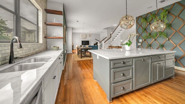 A modern kitchen with a large island, wooden flooring, and a dining area in the background. - THE PARKER, A Modern Retreat Near Everything: 3 BR, 3.5 bathroom house Sleeps 8 (Houston)