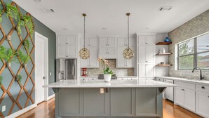 A kitchen with white cabinets, a large island, hanging pendant lights, and a brick backsplash. - THE PARKER, A Modern Retreat Near Everything: 3 BR, 3.5 bathroom house Sleeps 8 (Houston)