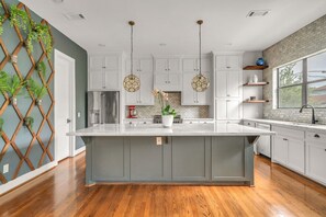 A kitchen with white cabinets, a large island, hanging pendant lights, and a brick backsplash. - THE PARKER, A Modern Retreat Near Everything: 3 BR, 3.5 bathroom house Sleeps 8 (Houston)