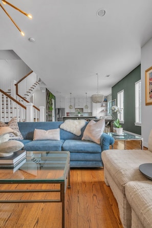 A modern living room with a blue sofa, wooden flooring, and a glass coffee table. - THE PARKER, A Modern Retreat Near Everything: 3 BR, 3.5 bathroom house Sleeps 8 (Houston)