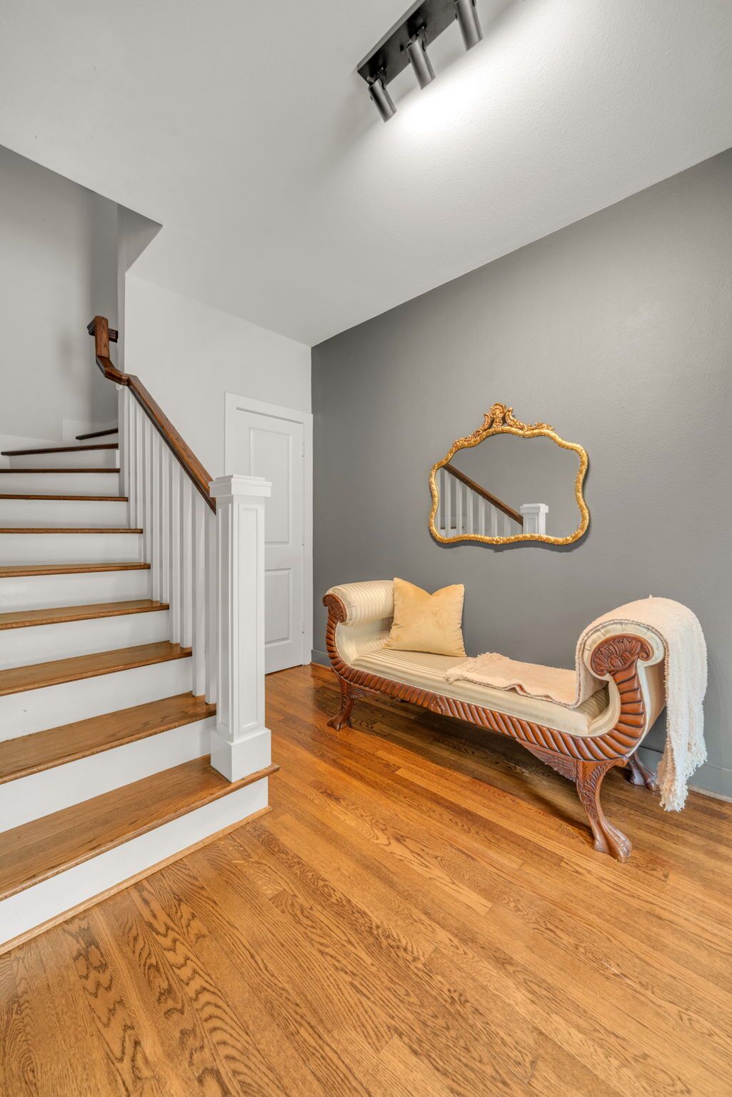 A staircase with wooden steps and white railings, a gray wall, a mirror, and a vintage sofa with a cushion.