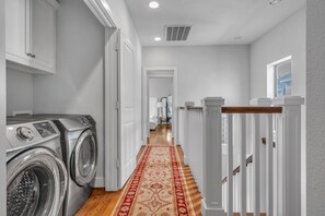 A laundry area with stacked washers and dryers, a wooden floor, and a red patterned rug. - THE PARKER, A Modern Retreat Near Everything: 3 BR, 3.5 bathroom house Sleeps 8 (Houston)
