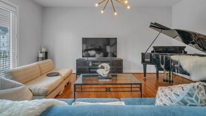 A living room with a grand piano, a sofa, a glass coffee table, and a modern chandelier. - THE PARKER, A Modern Retreat Near Everything: 3 BR, 3.5 bathroom house Sleeps 8 (Houston)