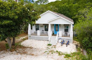 A white house with a blue door, a porch, and a small staircase leading to the entrance. There are bicycles parked in front. - 🦩Book Me Baby! Juan Sweet Beach House in Santa Rosa Beach🦩 (Santa Rosa Beach)