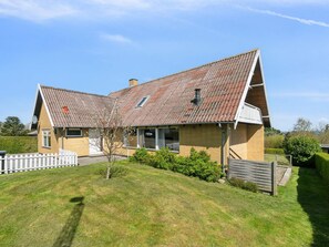 Ein zweistöckiges Haus mit geneigtem Dach, einer kleinen Veranda und einem weißen Zaun.