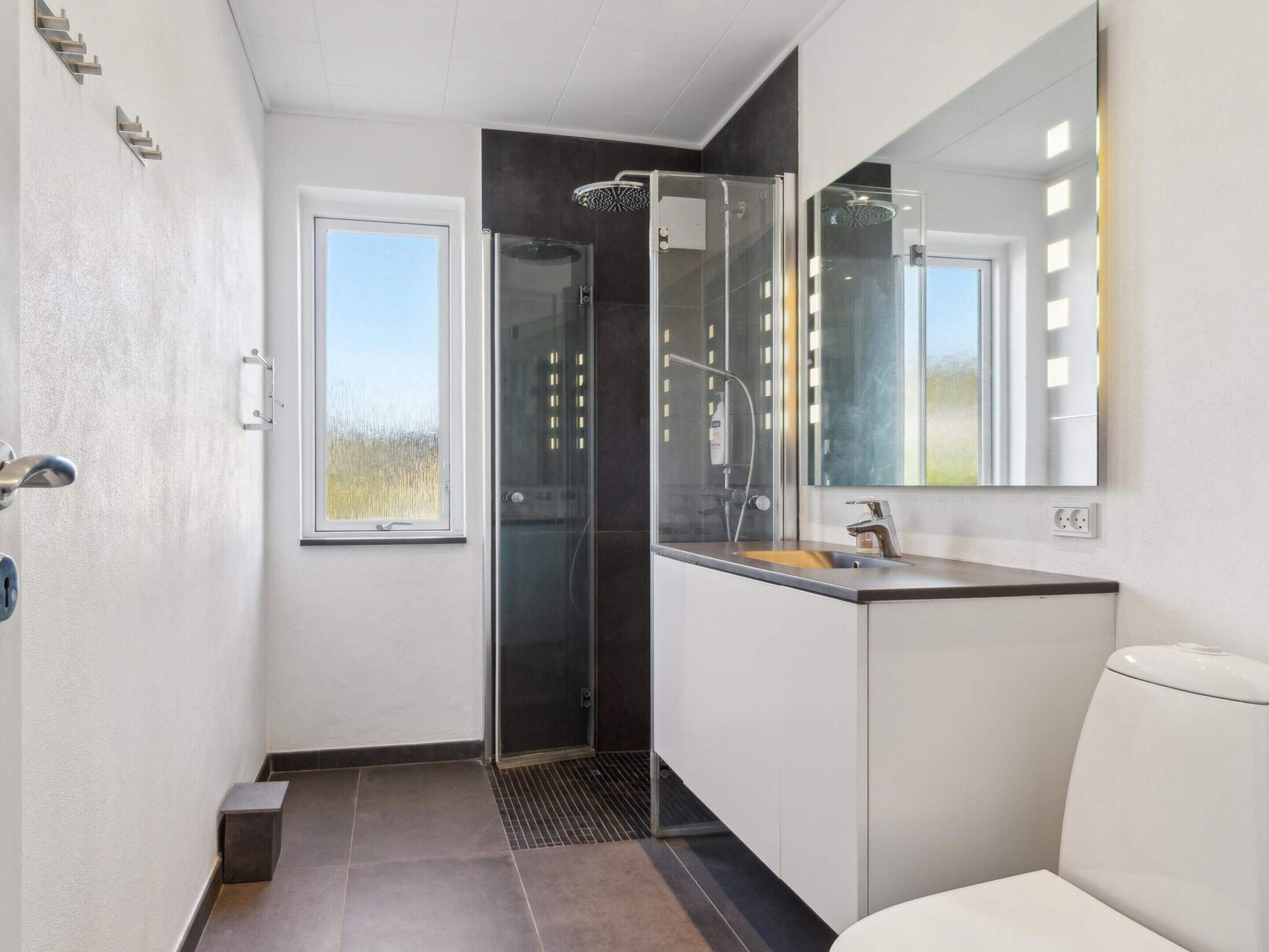 Moderni kylpyhuone, jossa on lasiseinäinen suihkukaappi, peilillä varustettu pesuallas ja wc.