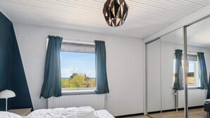 A bedroom with a bed, a window with curtains, a mirror, and a ceiling light fixture. - 5 Star Holiday Home in Allinge (Allinge)