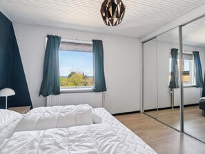 Ein Schlafzimmer mit einem Bett, einem Fenster mit Vorhängen, einem Spiegel und einer Deckenleuchte.
