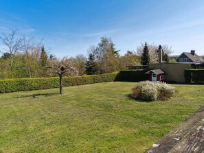 Ein grünes Rasenstück mit einem kleinen Schuppen, einer Hecke und einem Gebäude mit Schornstein im Hintergrund.