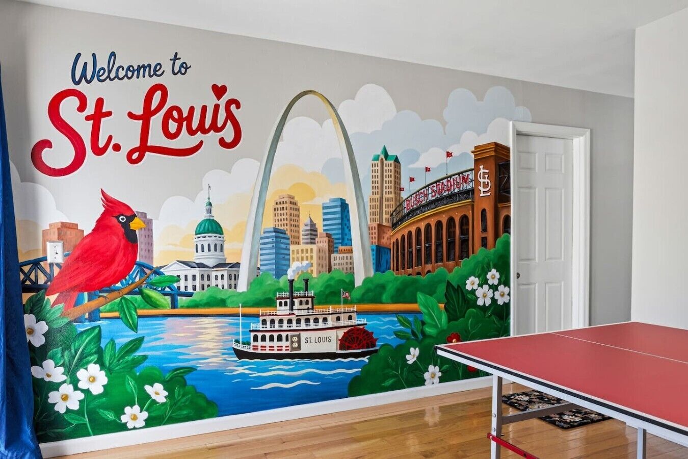 Habitación con un mural que muestra puntos emblemáticos de St. Louis, una mesa de ping pong roja y una puerta.
