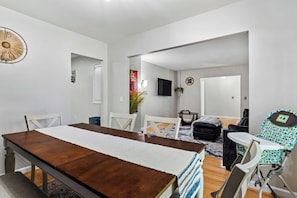 A modern living room with a dining table, chairs, a sofa, a baby rocker, and a TV.