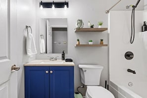 A bathroom with a white sink, blue cabinets, a toilet, a shower, and a shelf with plants. - Perfect for Families, Pet Friendly, Games Room (Ballwin)