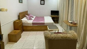 Een slaapkamer met een bed, een televisie, een klein tafeltje, een bank, gordijnen en een plafondlamp.