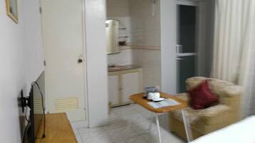 Hotellihuone, jossa on sänky, pieni pöytä, jossa on kuppi, tuoli, vaatekaappi ja ilmastointilaite.