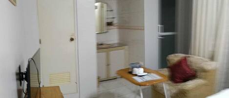 Habitación de hotel con cama, una mesita con una taza, una silla, armario y equipo de aire acondicionado.