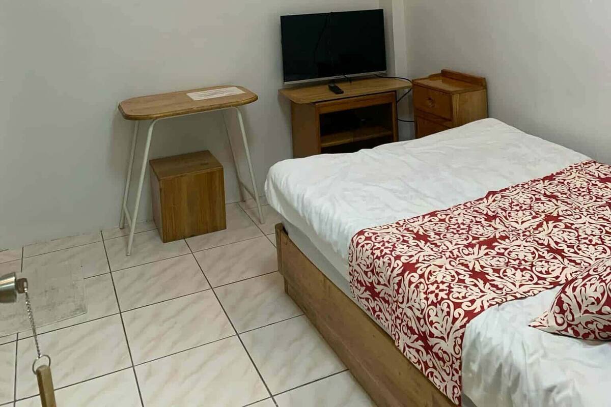 A bedroom with a bed, a desk, a television, and a wall-mounted painting.