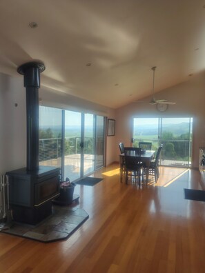 A spacious room with a wood-burning stove, large sliding glass doors, a dining table with chairs, and a ceiling fan.