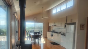A modern kitchen with a large island, a dining area with chairs, and a view through large windows. - Whole House in Toora on 2 ha. elevated with incredible views to Wilsons Prom (Toora)