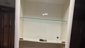 Een kamer met een witte kast, een glazen plank en een tafelkleed met bloemen.