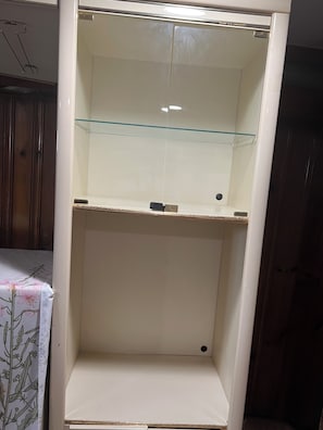 Ein Zimmer mit einem weißen Schrank, einer Glastrennwand und einer Tischdecke mit Blumenmuster.