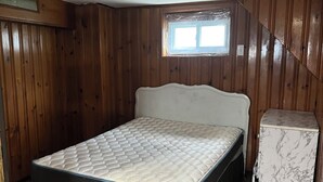 Een slaapkamer met een bed, een kleine koelkast, houten wanden, een raam en een visgraatvloer.