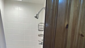 Een badkamer met witte betegelde wanden, een douche met handdouche en een houten deur met blauwe slotplaat.