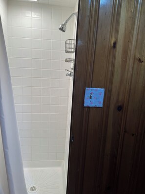 Ein Badezimmer mit weißen Fliesenwänden, einer Dusche mit Duschbrausehandstück und einer Holztür mit blauem Schloss.