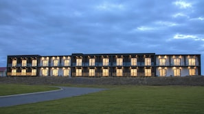 Un edificio moderno de varios pisos con balcones y grandes ventanales, rodeado de un césped cuidado y un camino de entrada pavimentado.