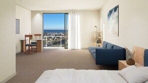 A hotel room with a bed, a blue sofa, a desk with a chair, a large window with a view of the city, and a painting on the wall. - Joy 40 Apartments Oamaru (Oamaru)