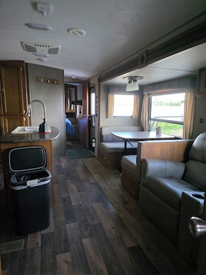 A compact RV interior with a kitchenette, a dining area, and a seating space.