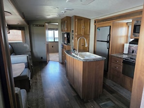 A compact RV kitchen with wooden cabinets, a sink, a stove, and a refrigerator.