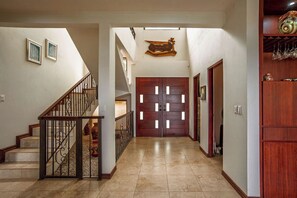 A hallway with a wooden staircase, a double door with a decorative design, and a shelf with glassware.