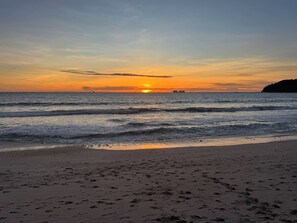 Ein Strand mit Sonnenuntergang, Wellen und einer entfernten Insel.