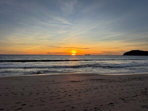 Una platja amb petjades que condueixen a l'aigua, un tramunt al fons i una illa a la distància.