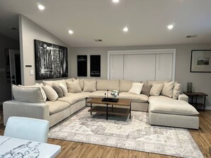 Ein Wohnzimmer mit einem Ecksofa, einem Couchtisch, einem gemusterten Teppich und einem großen abstrakten Gemälde an der Wand.