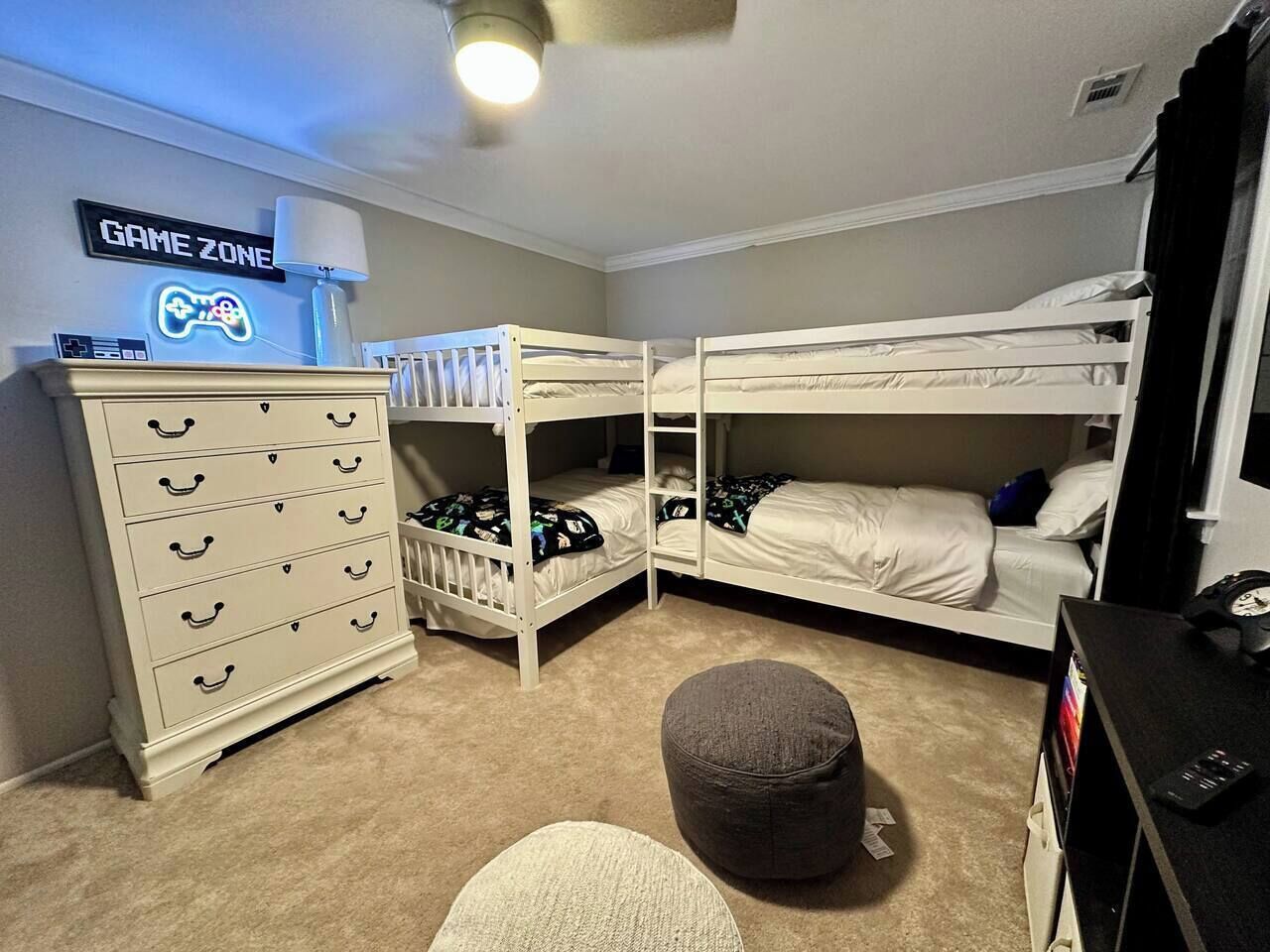 Ein Schlafzimmer mit Etagenbetten, einem Schminktisch, einem Schreibtisch mit Computer und einem Neon-Schild mit der Aufschrift 'GAME ZONE'.