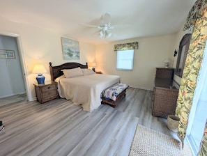 Ein Schlafzimmer mit einem Bett, Deckenventilator, Nachttisch mit Lampe, Fenster und Tür.
