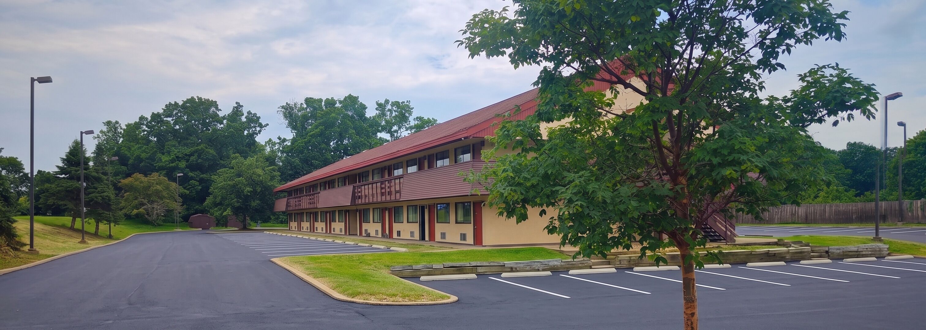 A motel with a red roof, multiple rooms, and a parking lot.