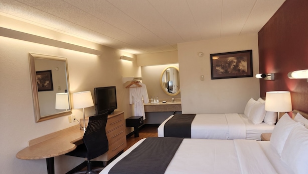 Une chambre d’hôtel avec deux lits, un bureau, une chaise, une télévision, un miroir, un peignoir et une salle de bain équipée d’un lavabo et d’un miroir.