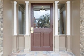 Eine braune Tür mit Fensterglas, gesäumt von weißen Säulen, und ein steinbelagter Eingangsbereich.