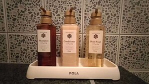 Casa de banho com área de chuveiro e produtos de higiene: frascos de champô, condicionador e gel de banho.