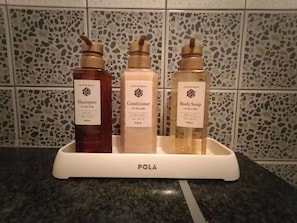 Un baño con estación de ducha que ofrece botellas de champú, acondicionador y jabón corporal.
