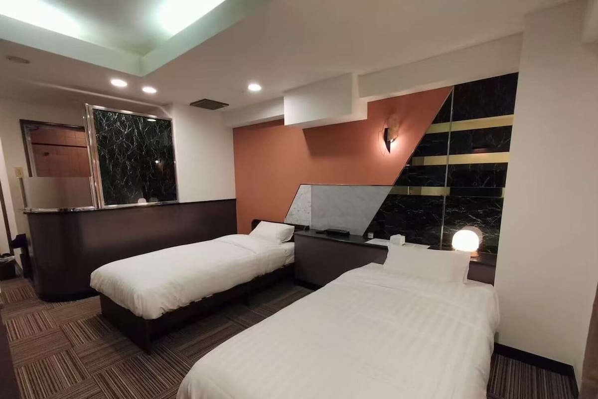 Una habitación de hotel con dos camas, una pared de mármol, una lámpara moderna y suelo de madera.