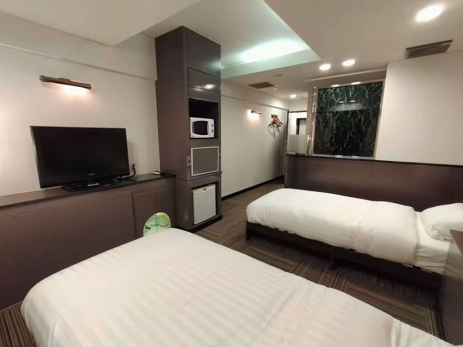 Ein Hotelzimmer mit Flachbildfernseher, Mikrowelle, Minikühlschrank, zwei Einzelbetten und einem großen Spiegel.