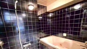 Casa de banho com paredes revestidas a mosaico preto, uma banheira branca e um chuveiro com chuveiro manual.