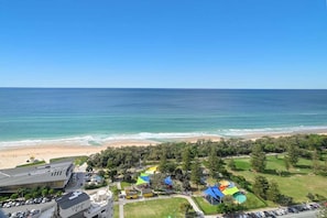 Ein Hotel an der Küste mit Blick auf den Strand, mehreren bunten Sonnenschirmen und einem Parkplatz.