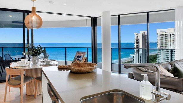 Una cocina moderna con vista al océano, un comedor con sillas de madera y un gran ventanal.