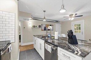 Eine moderne Küche mit Marmorarbeitsplatte, weißen Schränken, einem Einbauofen und einem Deckenventilator.