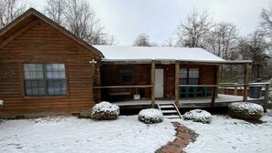 A wooden cabin with a porch, a window, and a snow-covered path leading to the entrance. - Dreams End Woodcliff Cabin (Connersville)