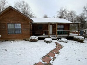 A wooden cabin with a porch, a window, and a snow-covered path leading to the entrance.